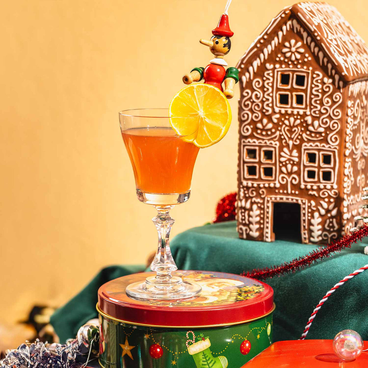 A Blueberry Gimlet cocktail garnished with a dried orange slice, styled with a gingerbread house