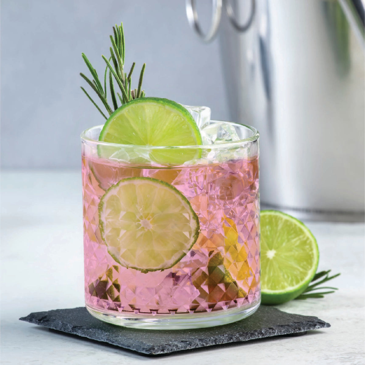 A pink cocktail garnished with lime slices and rosemary
