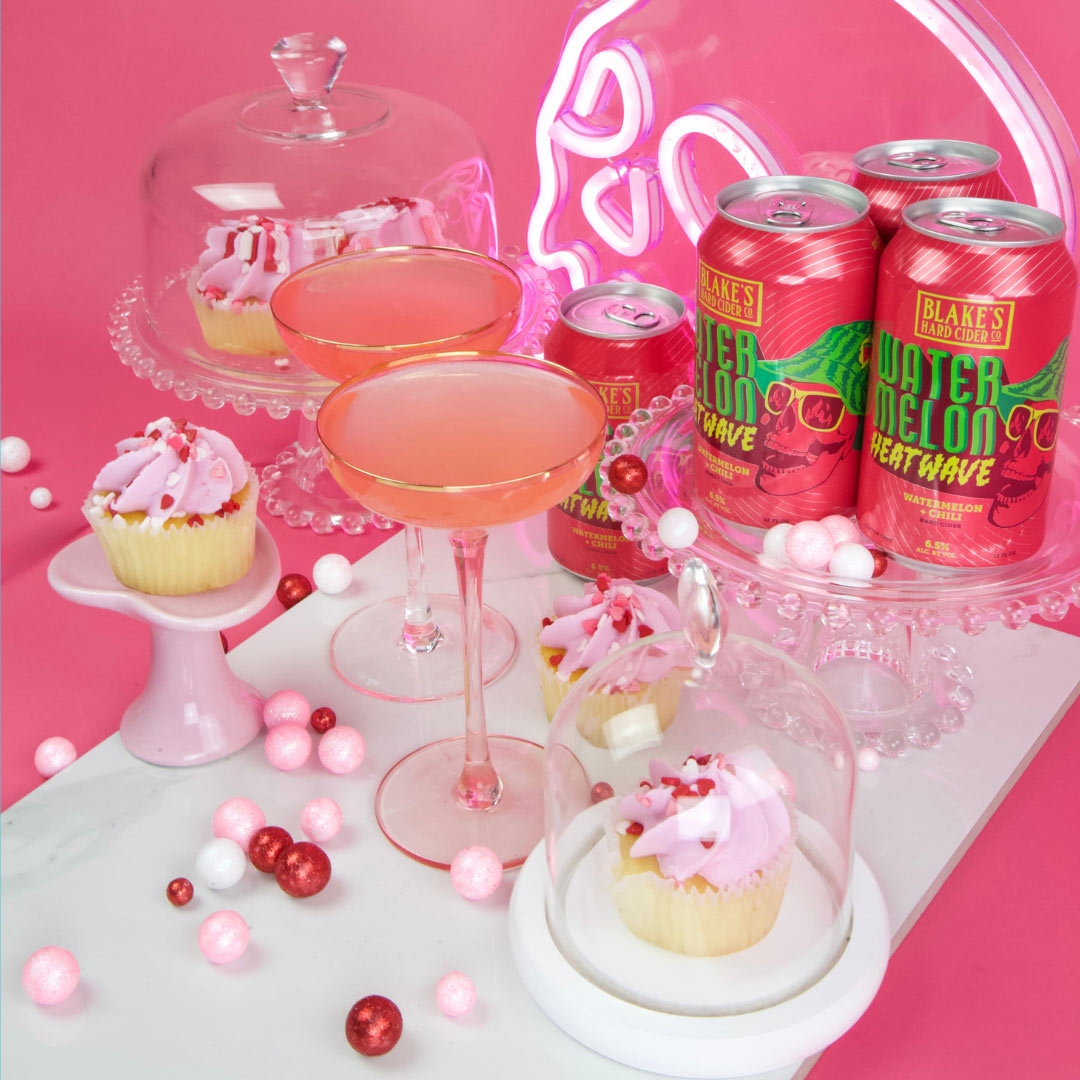 A pink Love Potion cocktail with cupcakes and cans of Blake's Watermelon Heatwave