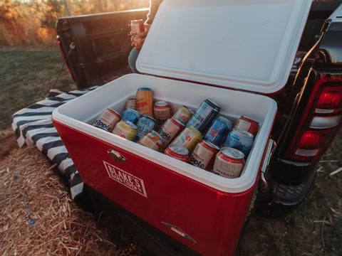 A cooler of Blake's Hard Cider cans in the back of a pickup truck at golden hour