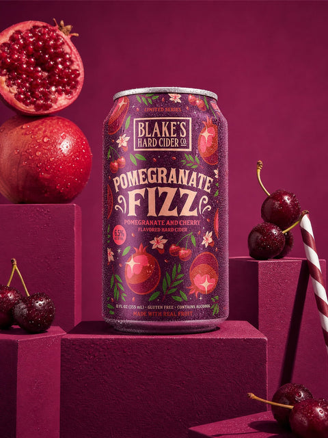 Blake's Hard Cider Pomegranate Fizz can on a red plinth with pomegranates and cherries